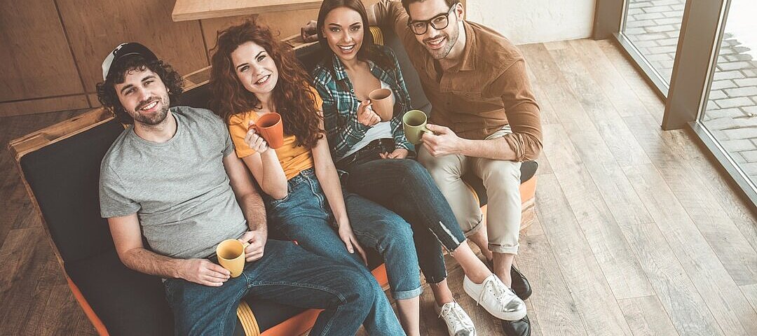 Draufsicht auf fröhliche junge Männer und Frauen, die Tee trinken und auf dem Sofa sitzen. © AdobeStock_ Yakobchuk Olena
