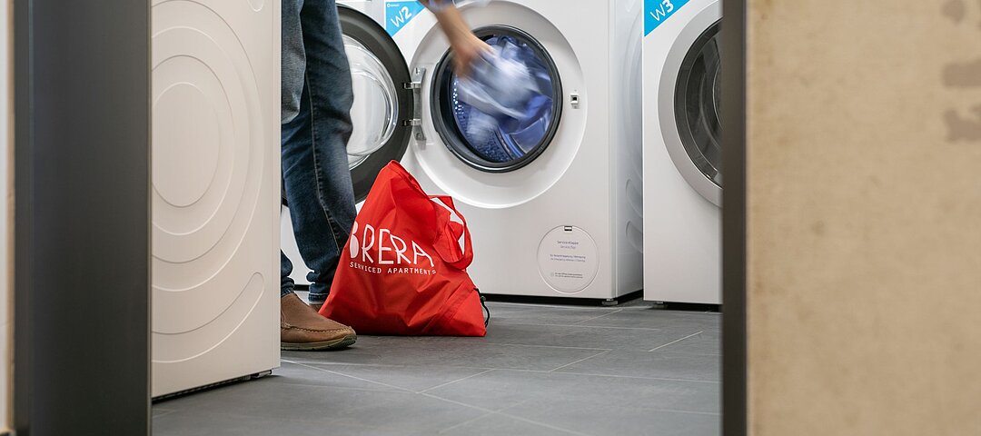 Waschmaschine wird mit Wäsche bestückt, roter Brera-Sack