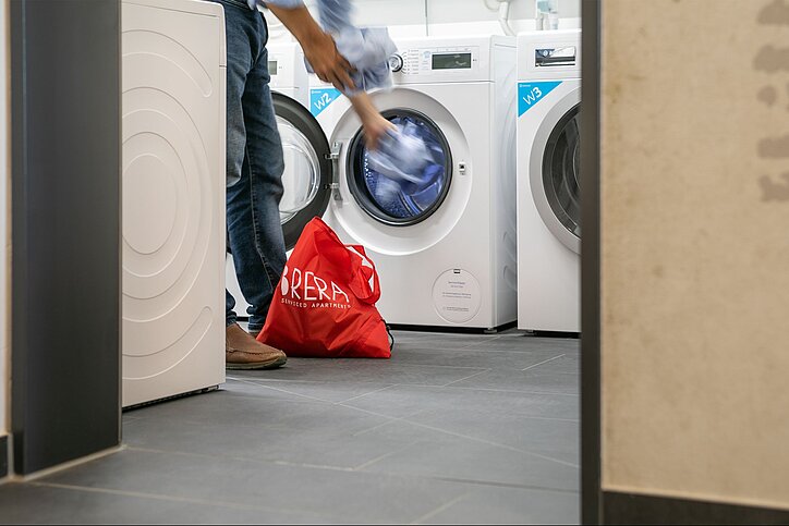 Waschmaschine wird mit Wäsche bestückt, roter Brera-Sack