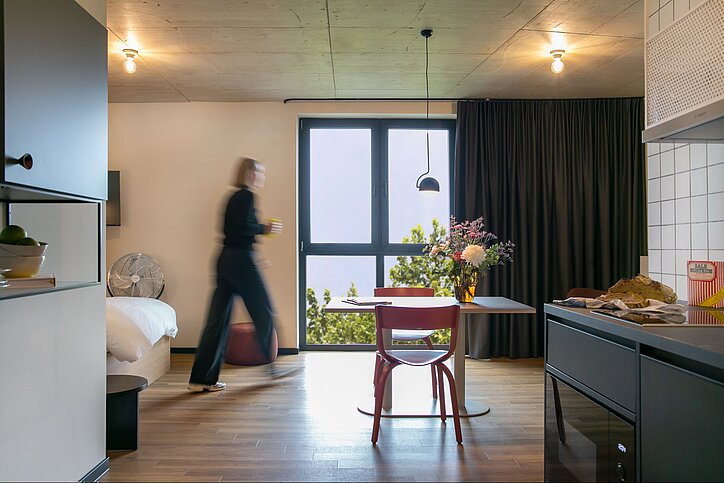 Stayery hat jetzt auch in der Ruhrstadt Bochum eine Adresse. Das Gebäude hatte Catella 2023 gekauft. © Stayery  Apartment mit Fenster, Tisch, Küchenzeile und einer Person, die durchläuft