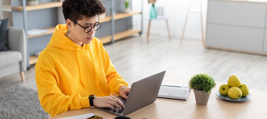 Student mit gelbem Hoody arbeitet konzentriert am Laptop.