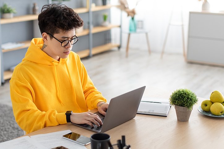 Student mit gelbem Hoody arbeitet konzentriert am Laptop.